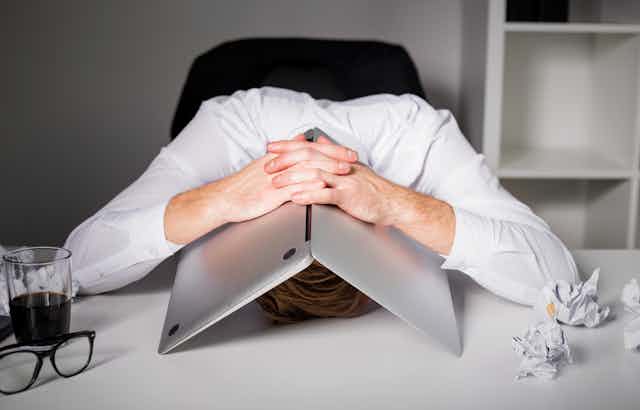 Man hiding under laptop with head on desk