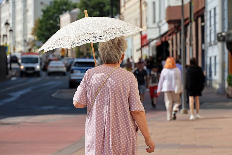 A senior woman walking with a sun umbrella.