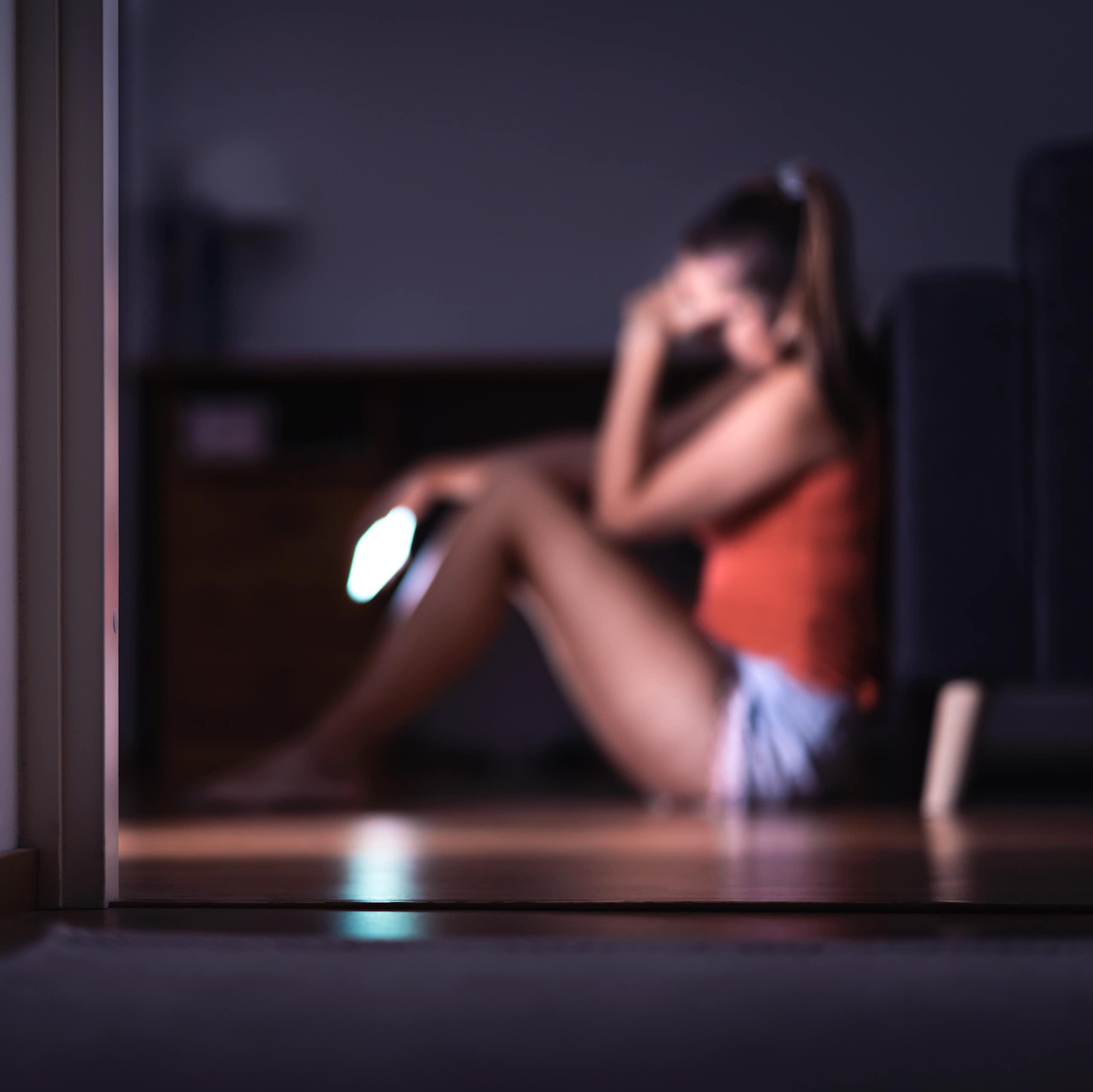 Woman sits on windowsill holding phone and looking worried