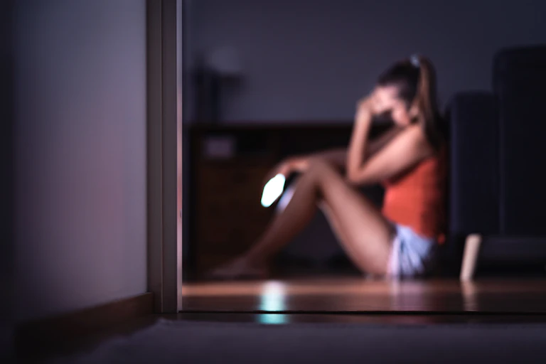 Woman sits on windowsill holding phone and looking worried