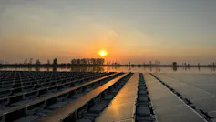 The sun sets over an expanse of water on which about 20 long solar panel systems are mounted
