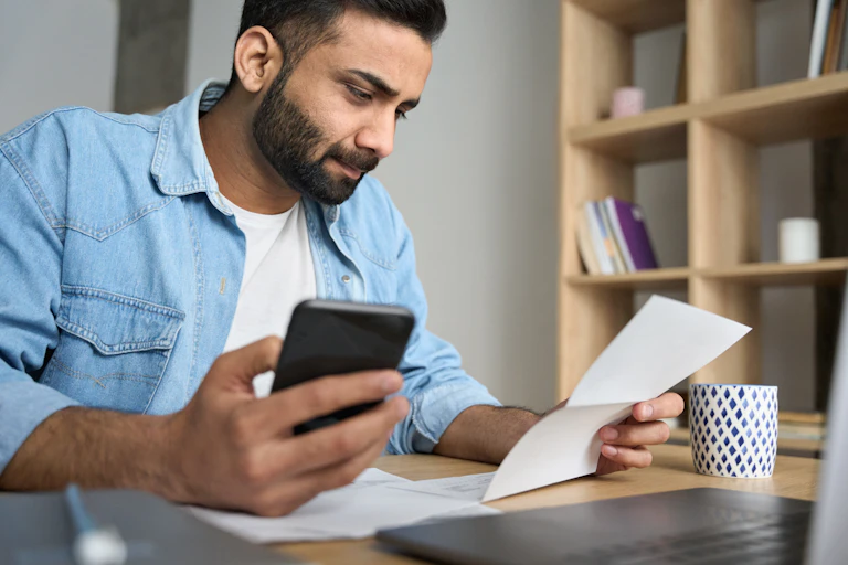 man using an app on his phone and looking at a bill