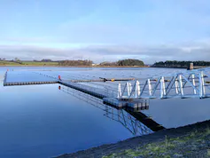 A metal footbridge from the land heads out to the middle of a lake where an array of solar panels are floating