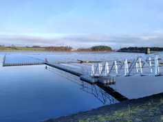 A metal footbridge from the land heads out to the middle of a lake where an array of solar panels are floating