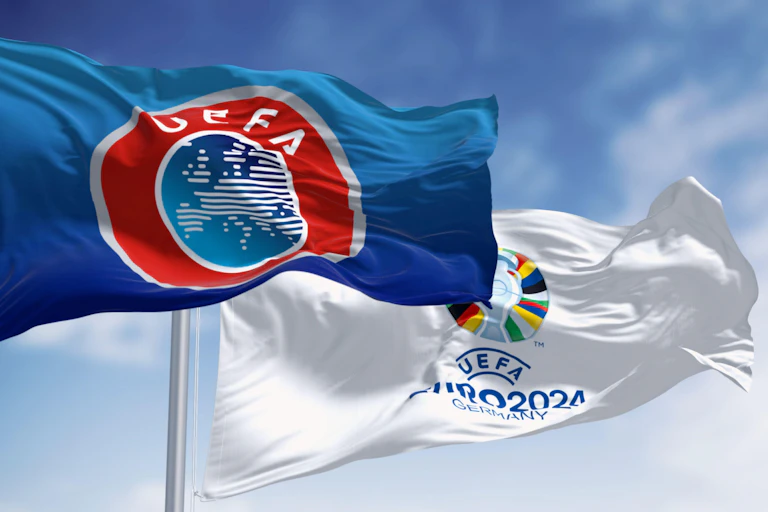 A Uefa flag and a Euro 2024 flag flying against a blue sky.