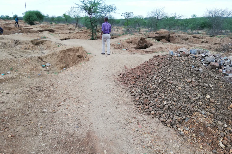 A gravel road with pits dug along the sides and mounds of earth piled up here and there