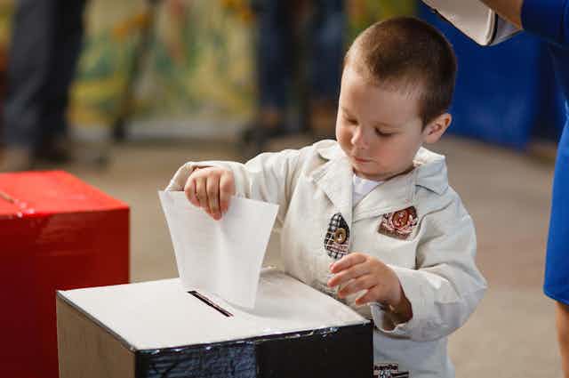 A young child putting a ballot into a box