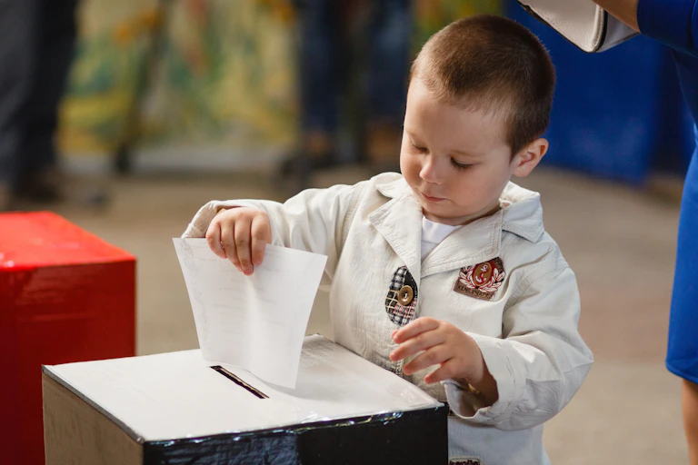 A young child putting a ballot into a box