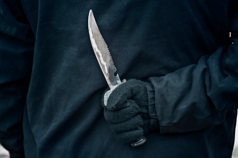A gloved hand holding a sharp knife behind the user's back