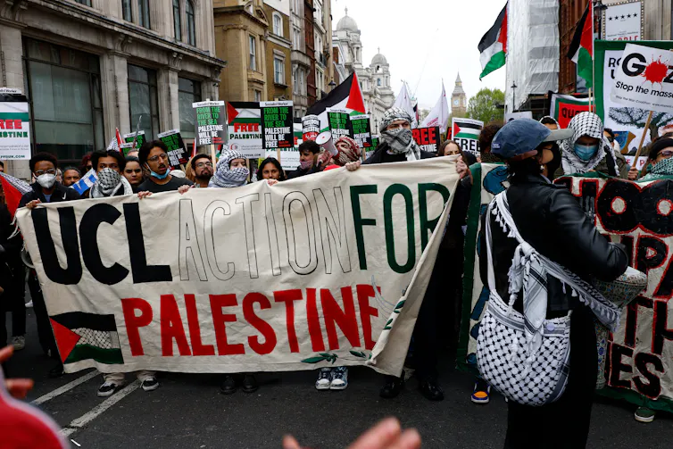 Participants in a protest march walking behind a large banner that reads 'UCL action for Palestine'