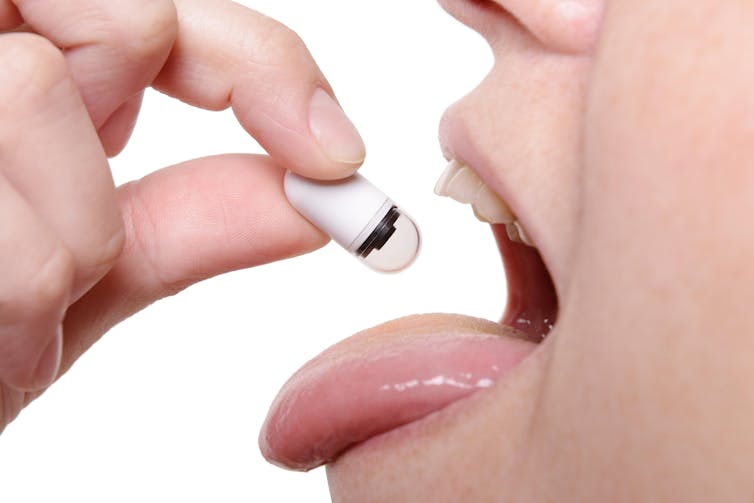 Close-up of person dangling pill-like device over tongue