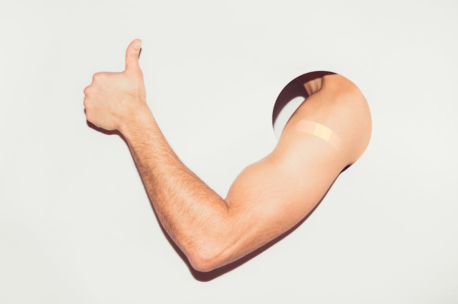 Muscular arm with bandaid on deltoid through through a hole, thumbs up