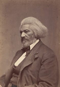 Un hombre negro con cabello gris viste un traje oscuro mientras posa para un retrato.
