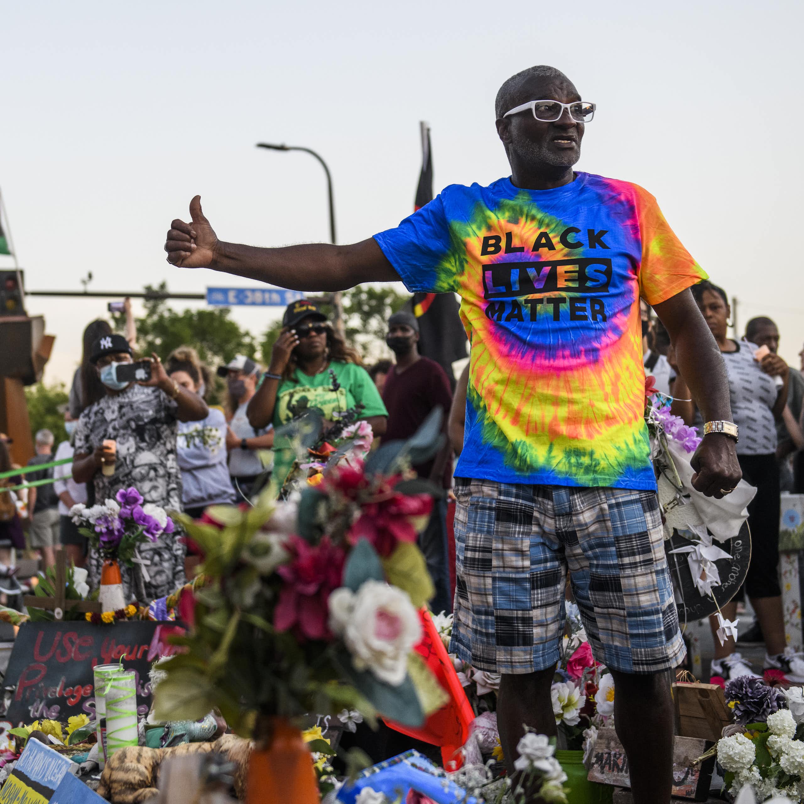 A man in a Black Lives Matter t-shirt talks to a large crowd outside.