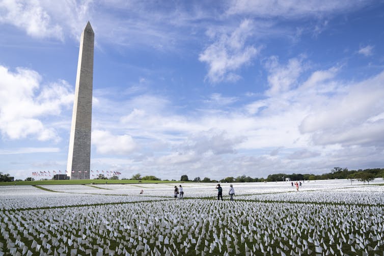 Acres of white flags are planted in the ground, behind them stands a large obelisk.