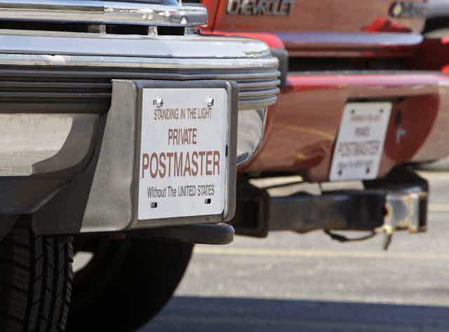 A close-up of a car with a sign in place of a license plate reading, in part 'Private postmaster without the United States.'