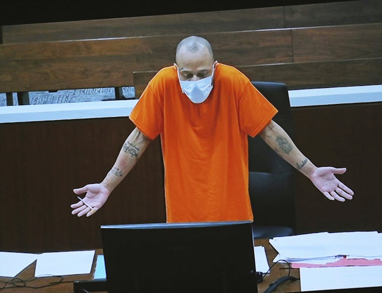 A man in an orange shirt holds his hands out to his sides.