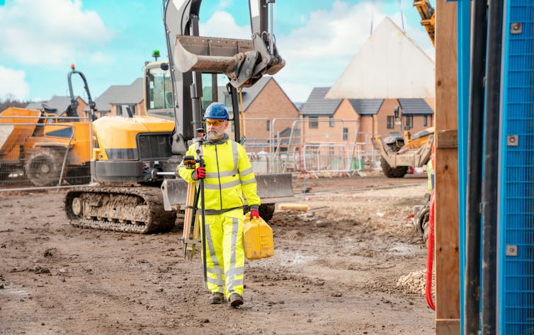 A builder on a partially constructed housing development in front of a digger.
