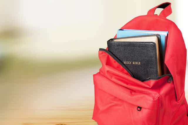 A red backpack, unzipped to show a Bible inside.