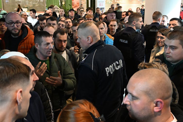A man in police uniform talks to a group of yoing men.