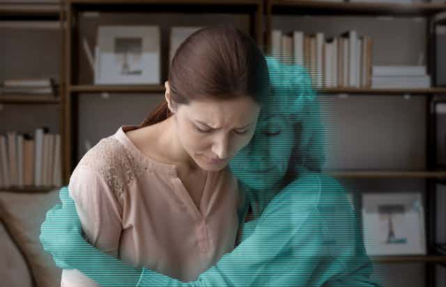Art concept: a grieving woman is hugged by a blue digital avatar of her mother.