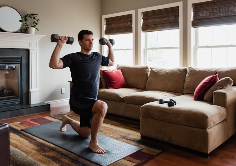 A man does weighted lunges in his lounge room.