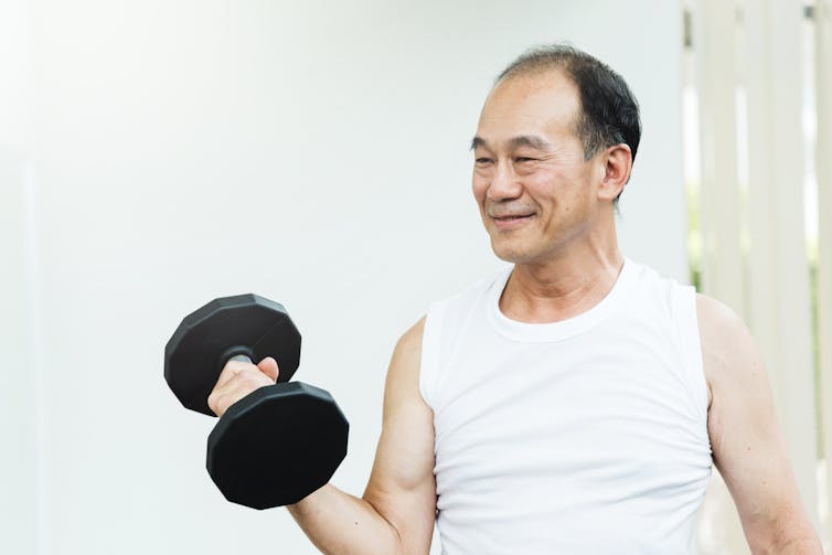 An older Asian man lifts weights at home.