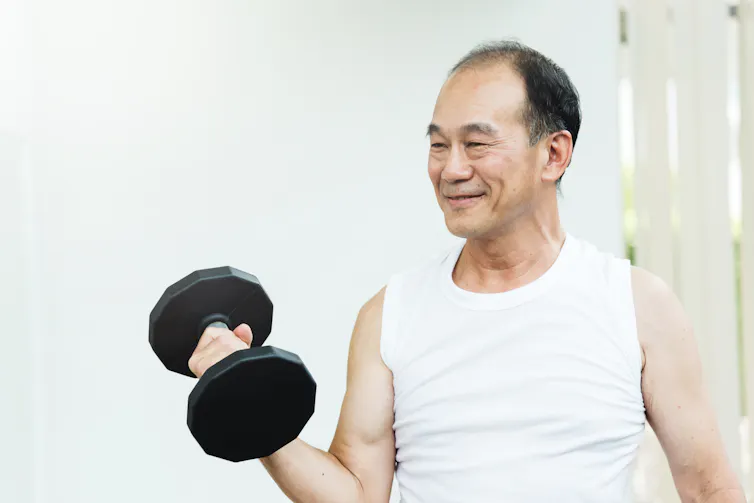 An older Asian man lifts weights at home.