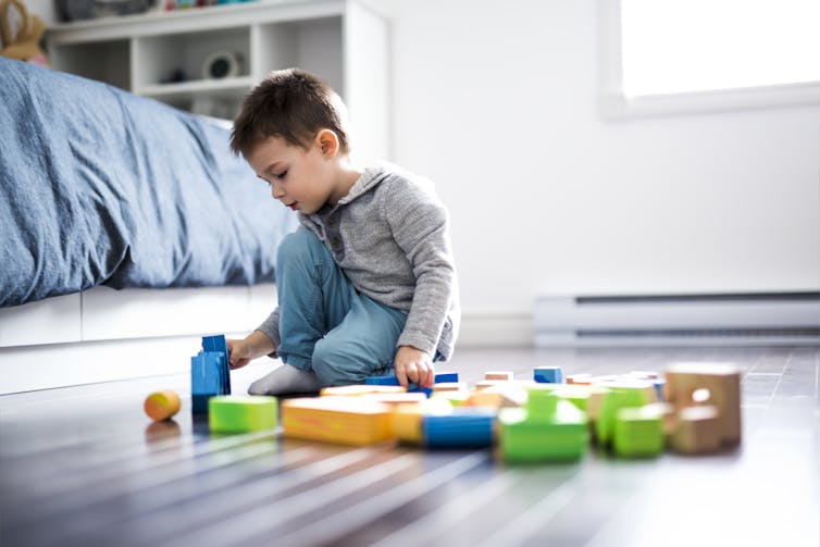 A boy playing with toys on the floor of a bedroom.