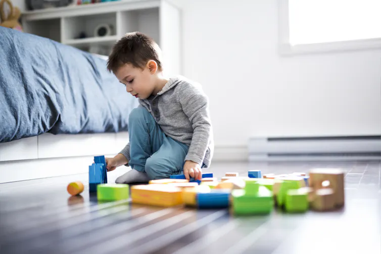 A boy playing with toys on the floor of a bedroom.
