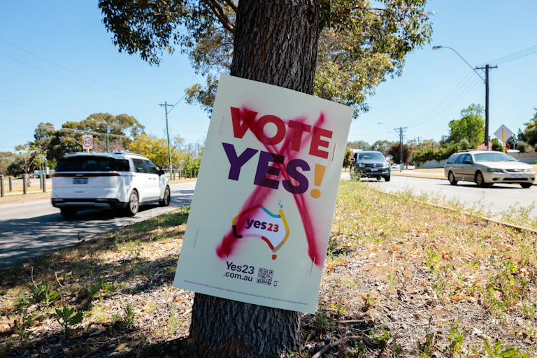 A sign that reads vote yes with a red graffiti X spraypainted on top