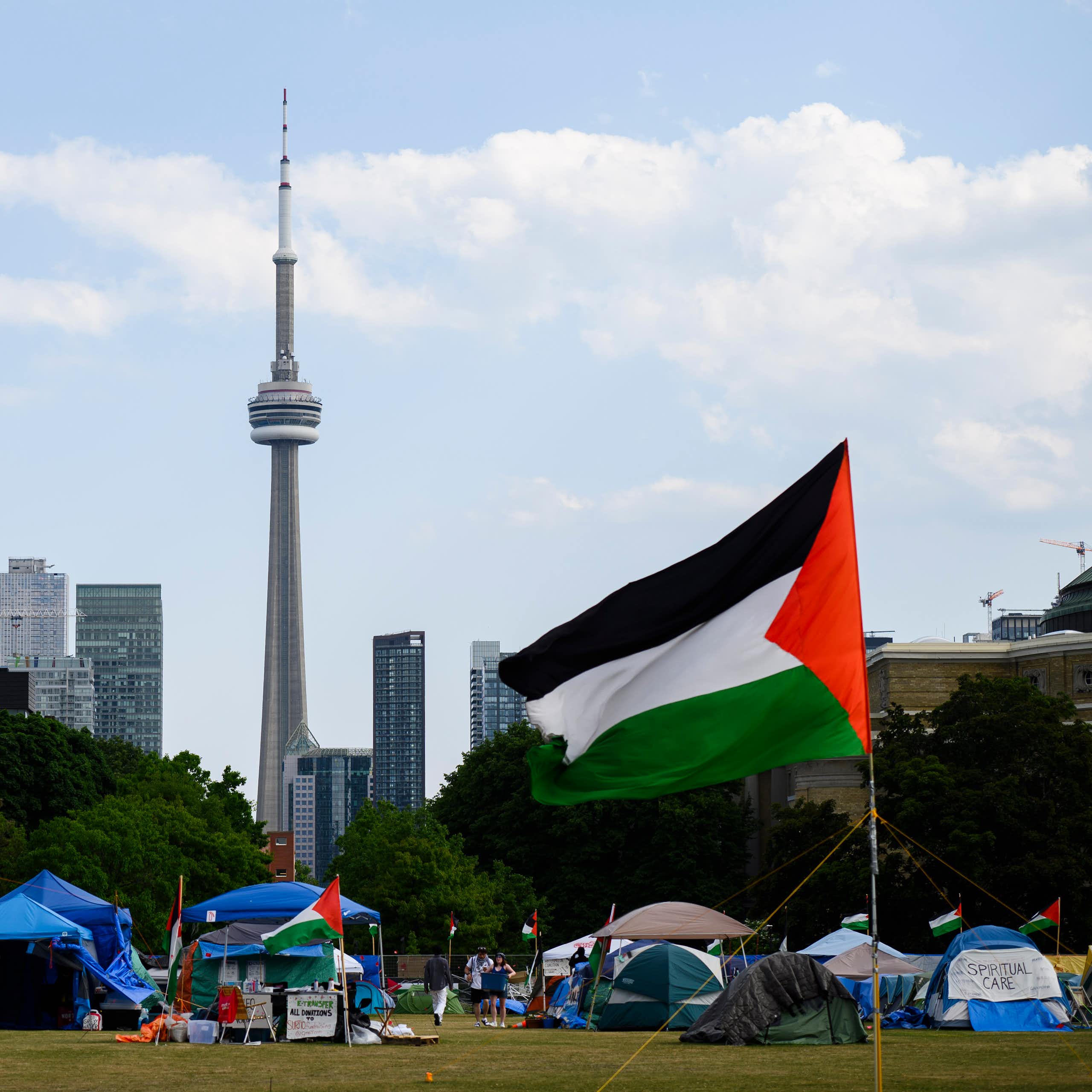 Tents on a lawn with Palestinian flags. The CN Tower and Toronto skyline are seen in the background
