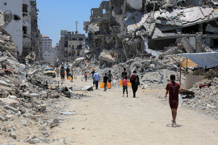 Palestinian people walk among the remains of buildings destroyed in an Israeli airstrike, JUne 12 2024.