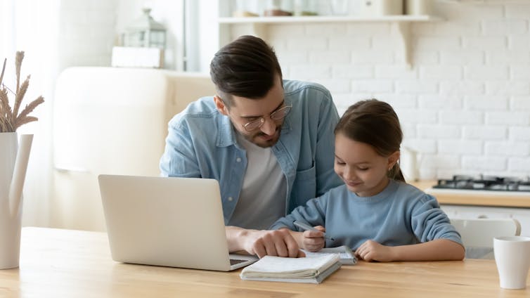 A young father helping his daughter with her homework at a kitchen table