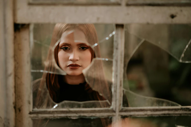 Woman looks through hole in broken window pane