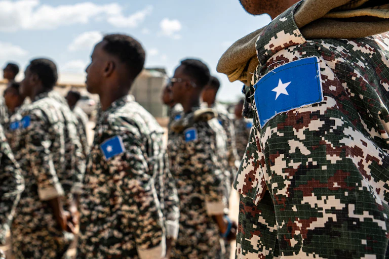 Men in camouflage uniforms with blue patches on their sleeves. A white star in the middle of the blue patch.