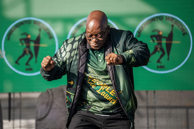 A man dances on stage wearing MK Party regalia.
