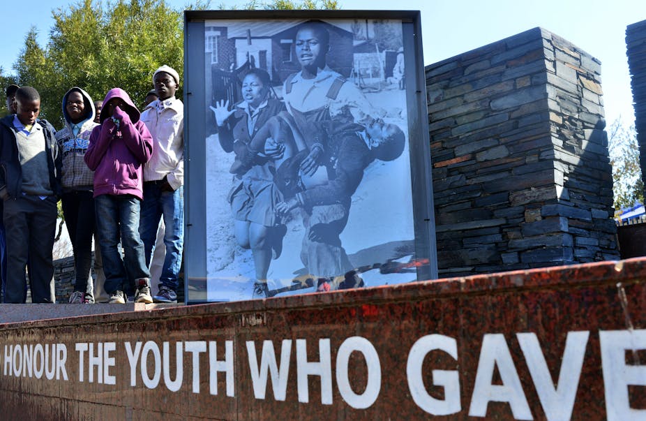 Young boys stand alongside a structure bearing a photo of a schoolboy being carried in the arms of another young man
