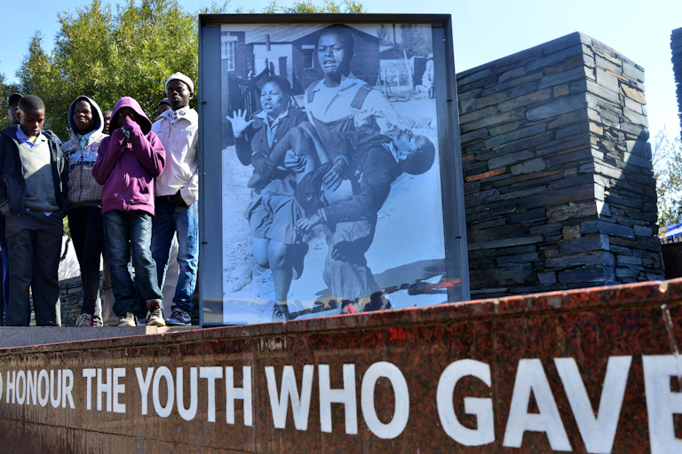 Young boys stand alongside a structure bearing a photo of a schoolboy being carried in the arms of another young man