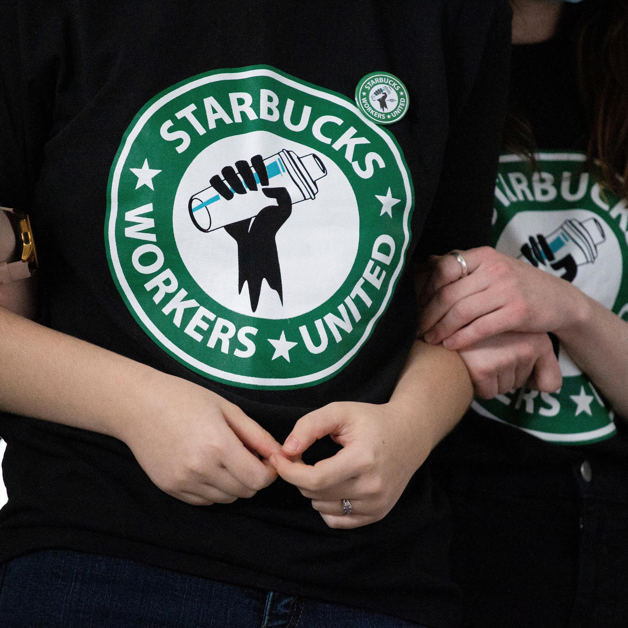 Starbucks employees and supporters link arms, with two wearing Starbucks Workers United t-shirts.