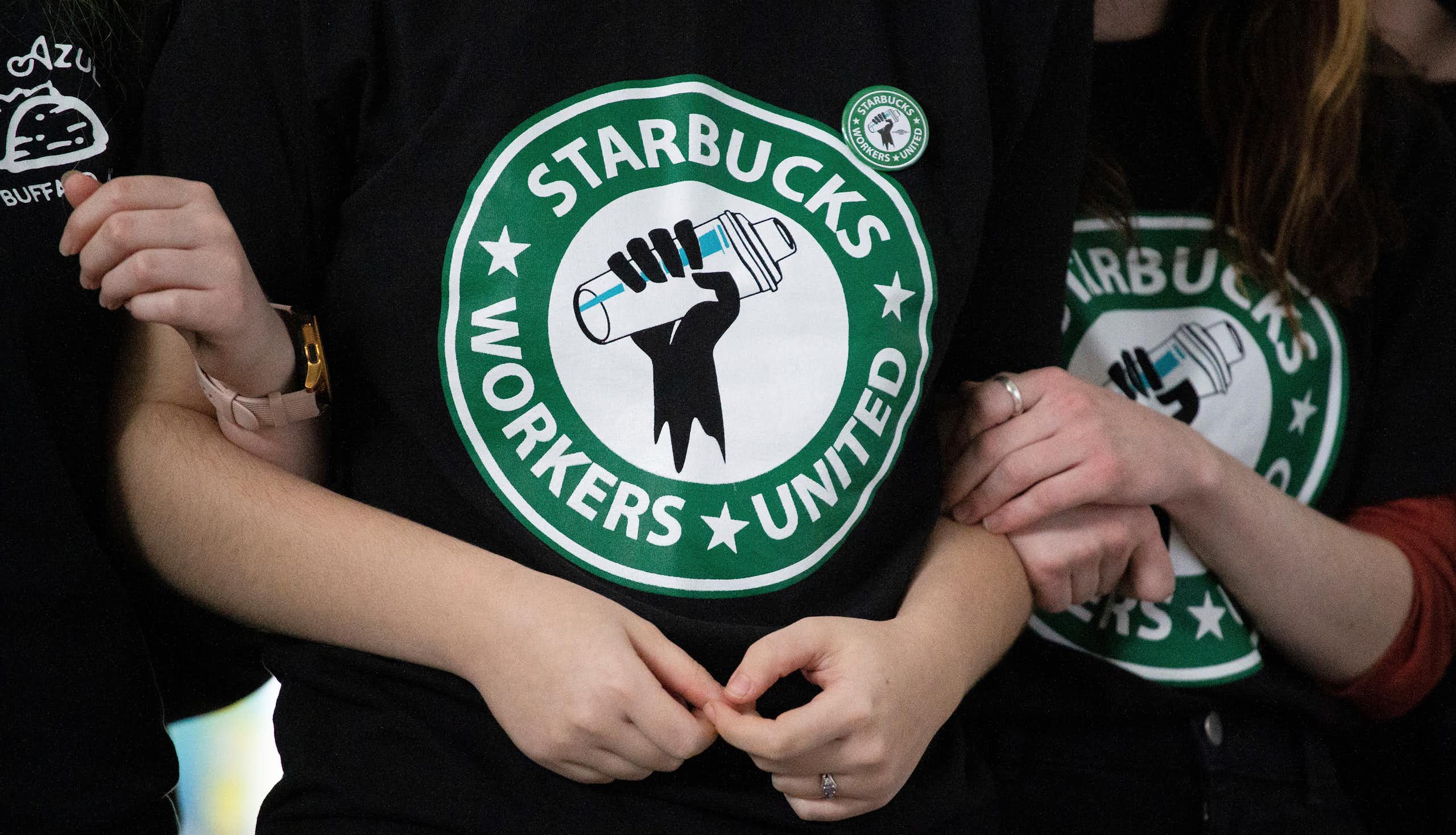Starbucks employees and supporters link arms, with two wearing Starbucks Workers United t-shirts.