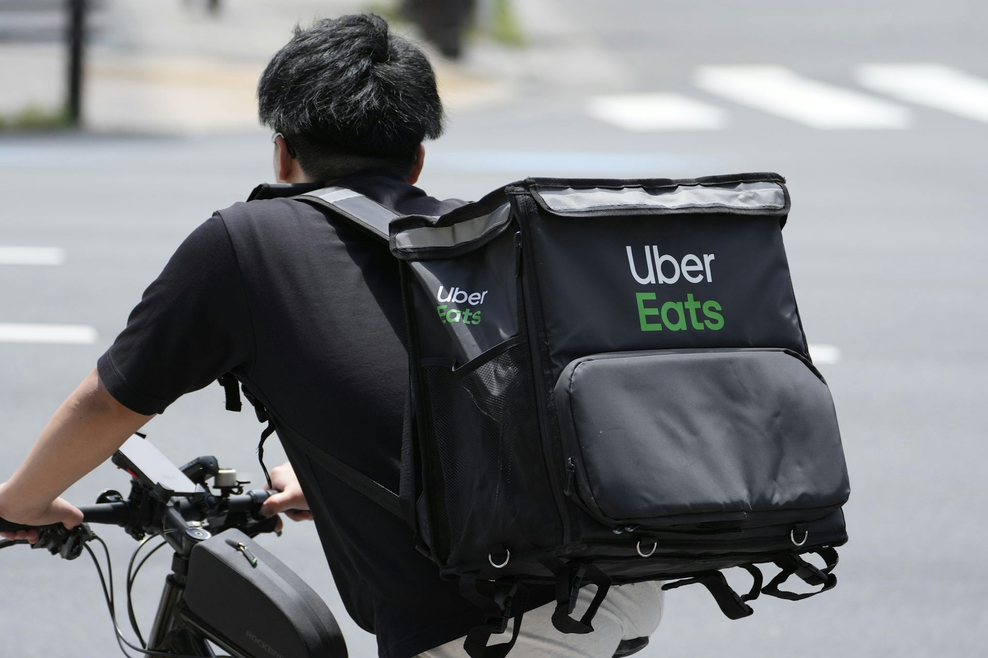 Rear view of a person with short hair riding a bike and wearing a backpack that says 'Uber Eats' on it