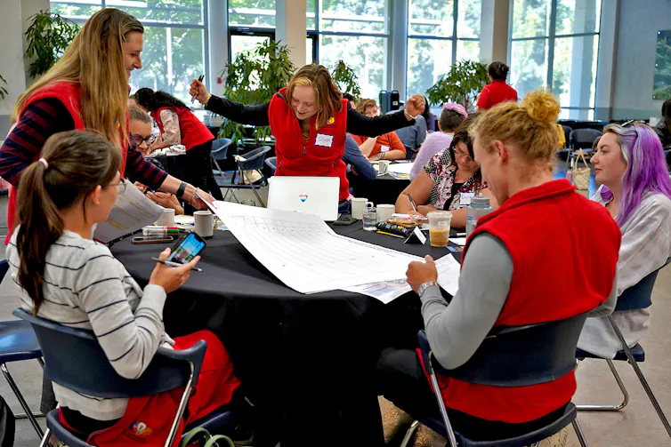 People wearing red vests sit at a round table