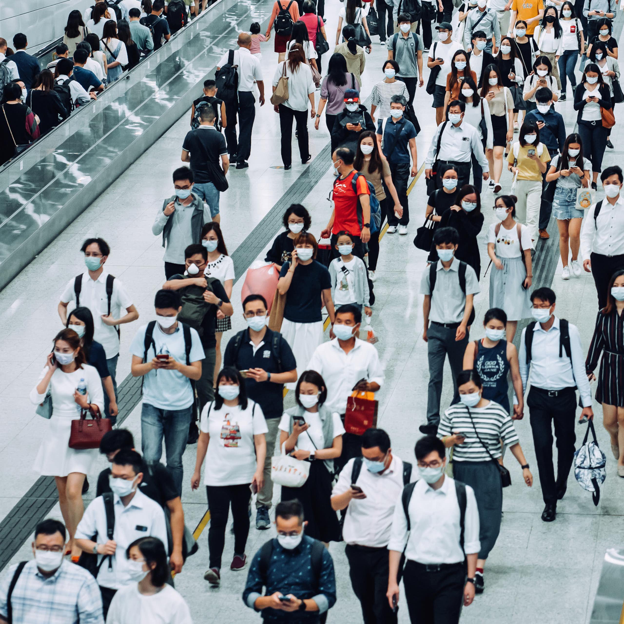 Crowd of busy commuters with face masks walking through platforms at a subway station