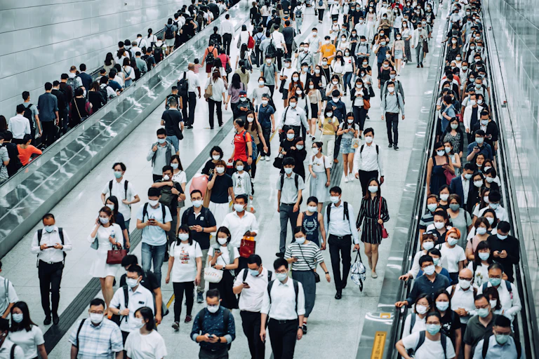 Crowd of busy commuters with face masks walking through platforms at a subway station