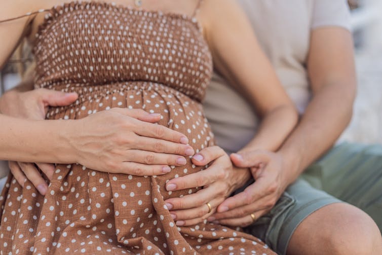 Pregnant woman sitting on lap of man, man's arms around woman's belly