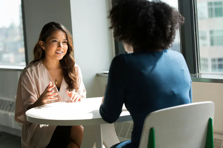 Woman interviews another woman sat at small table