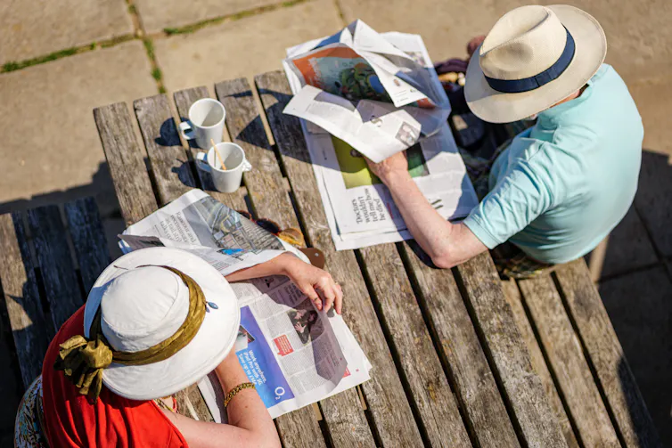 Overhead view of a couple in straw hats sitting at a picnic table reading the newspaper