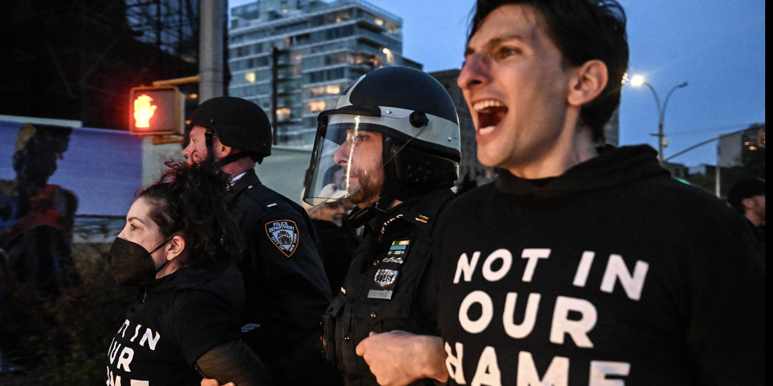 A man wearing a shirt that says 'NOT IN OUR NAME' is pulled away by police.