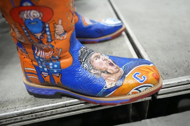 A closeup of an orange and blue painted cowboy boot with images of men's faces.